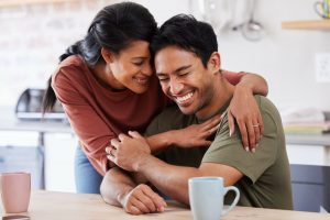 Couple, love and laugh with a man and woman hugging, laughing or having fun in the kitchen of their home together. Happy, smile and humor with a married male and female embracing in their house